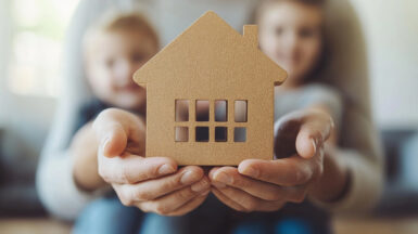 Une femme tien ces enfants dans ces bras et montre une maison dans ces mains