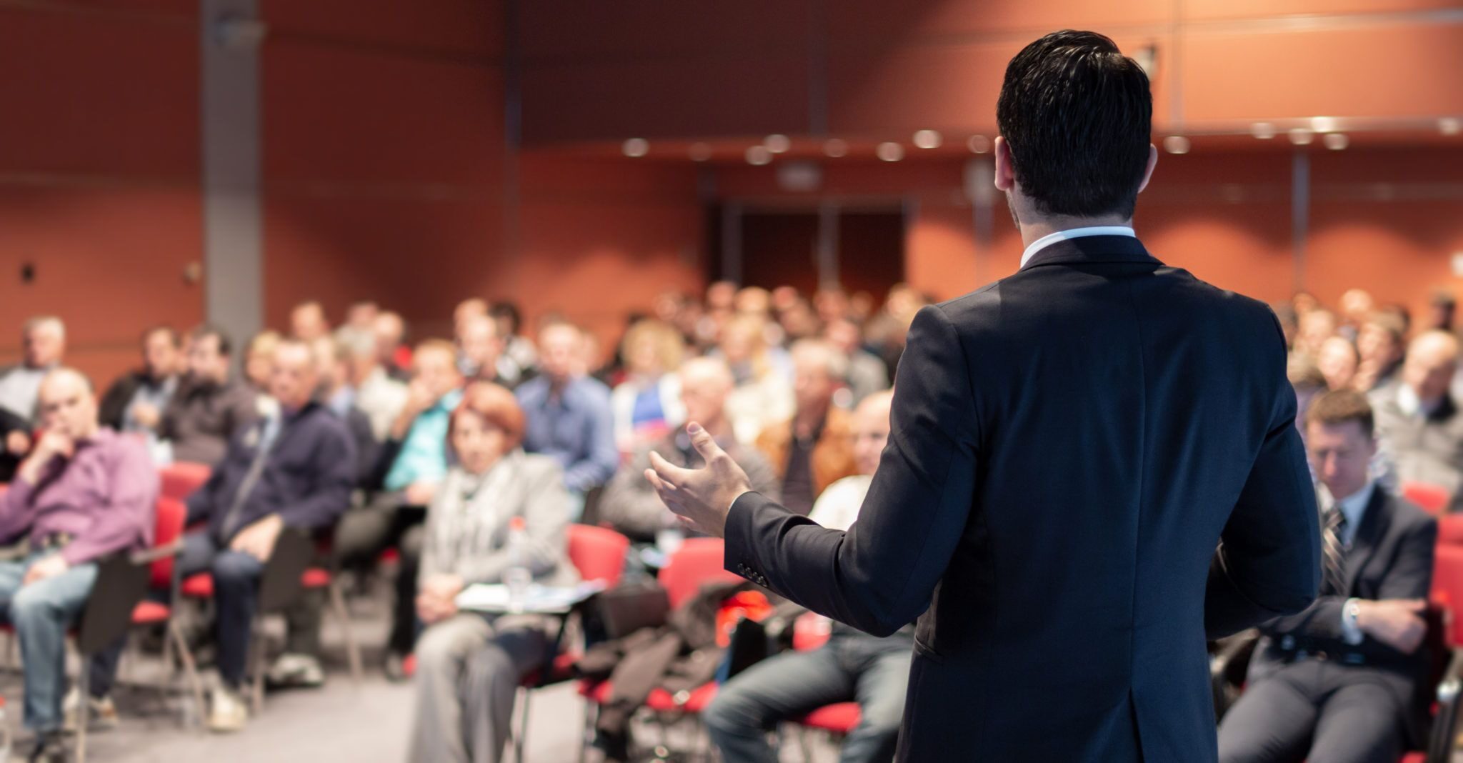 Homme de dos donnant une conférence face à un public de professionnels