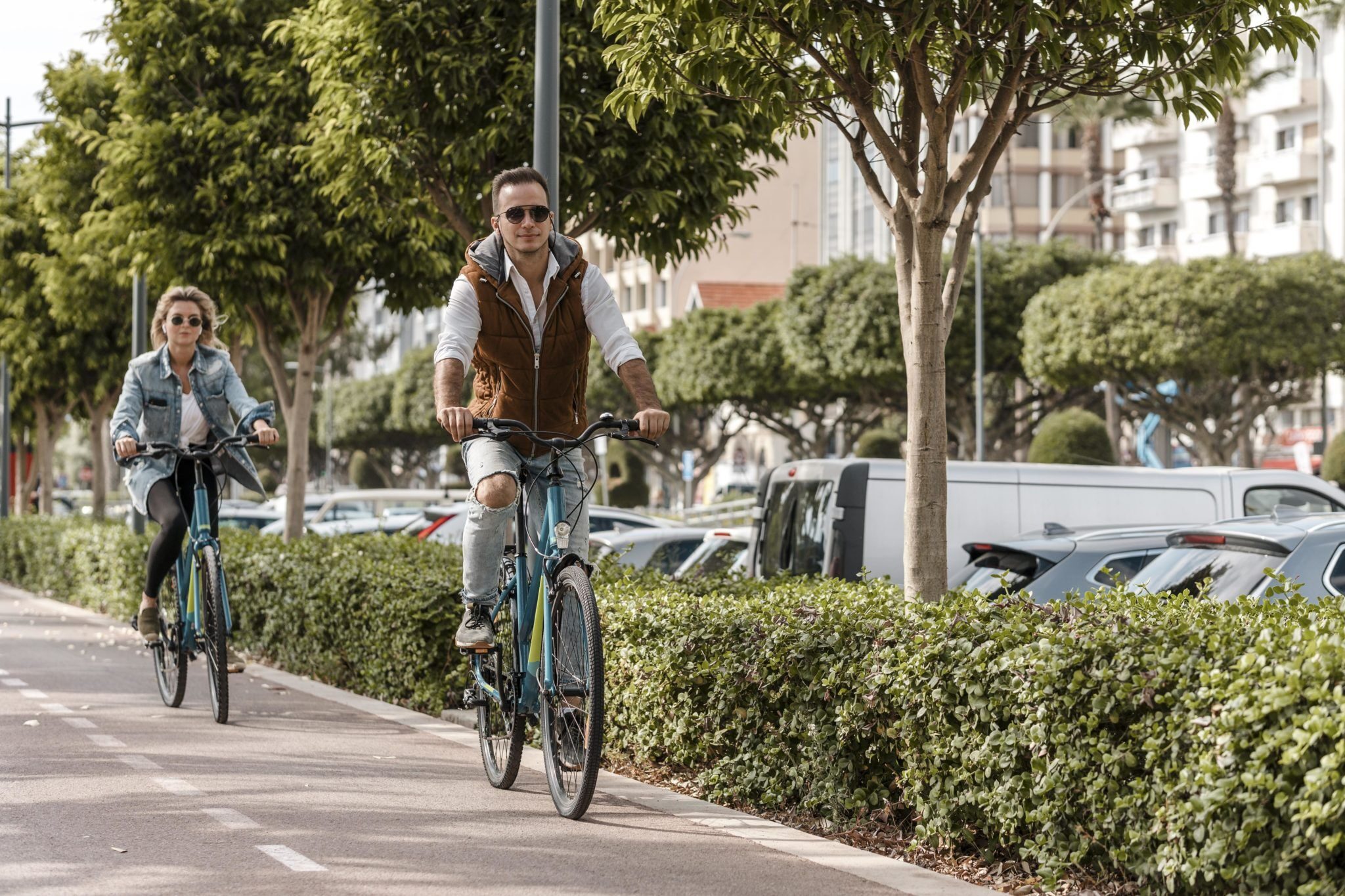 Un homme et une femme pédalent sur un piste cyclable, le long d'une rue animée