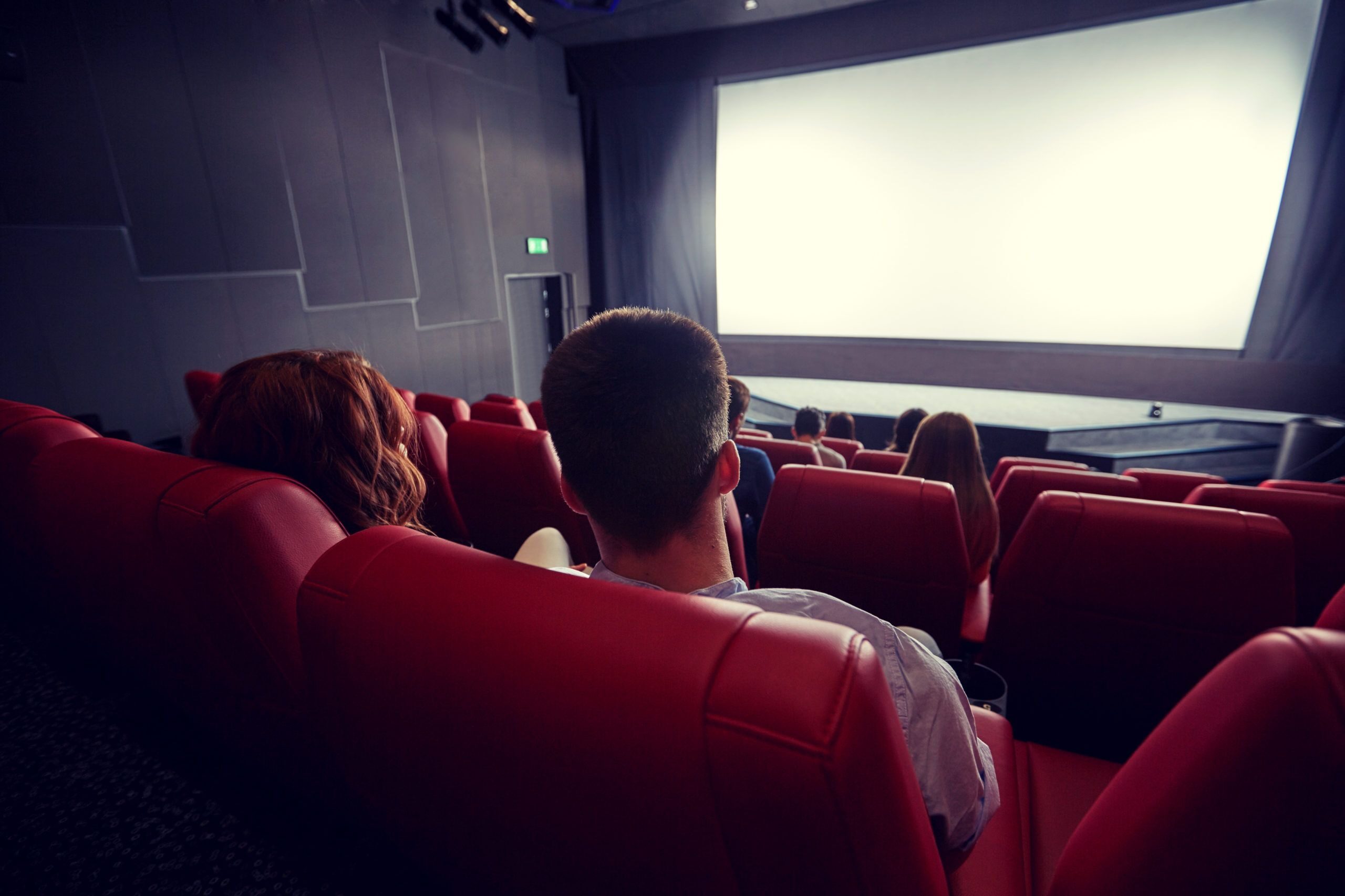 Vue d'un écran de cinéma depuis le haut de la salle, derrière les sièges