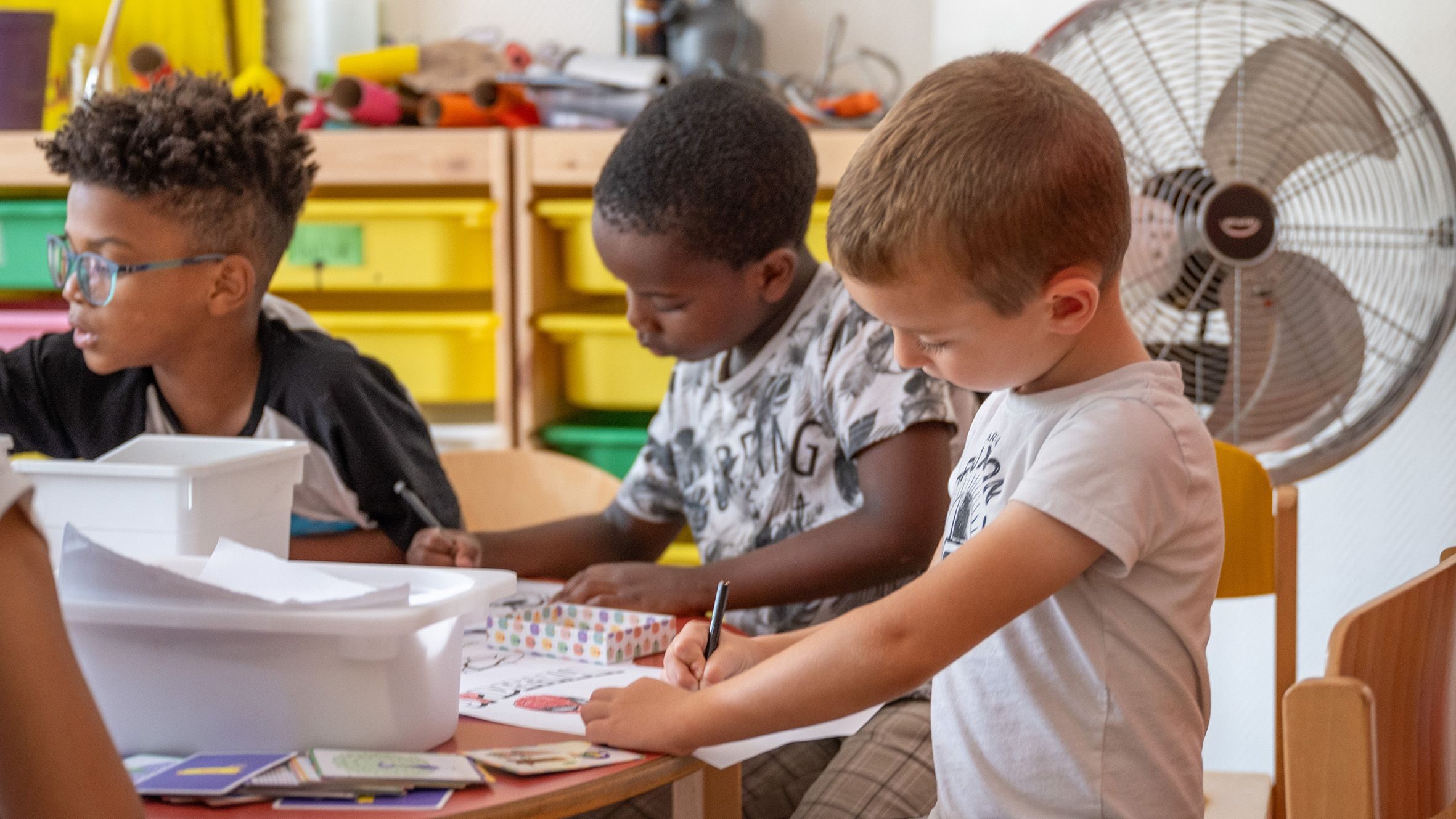 de jeunes enfants assis à une table qui font du coloriage