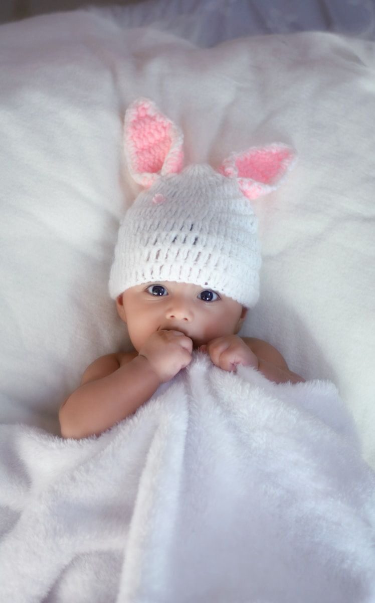 bébé en bonnet allongé sur du textile blanc