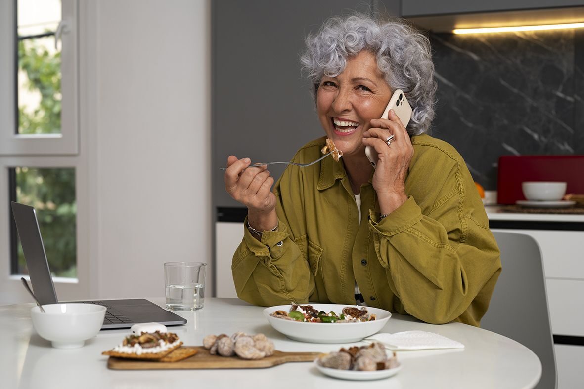 Une femme senior mange une salade tout en répondant au téléphone