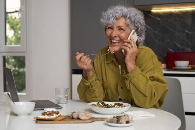 Une femme senior mange une salade tout en répondant au téléphone