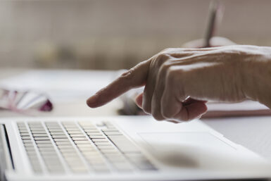 une main de personne âgée au-dessus d'un clavier de portable