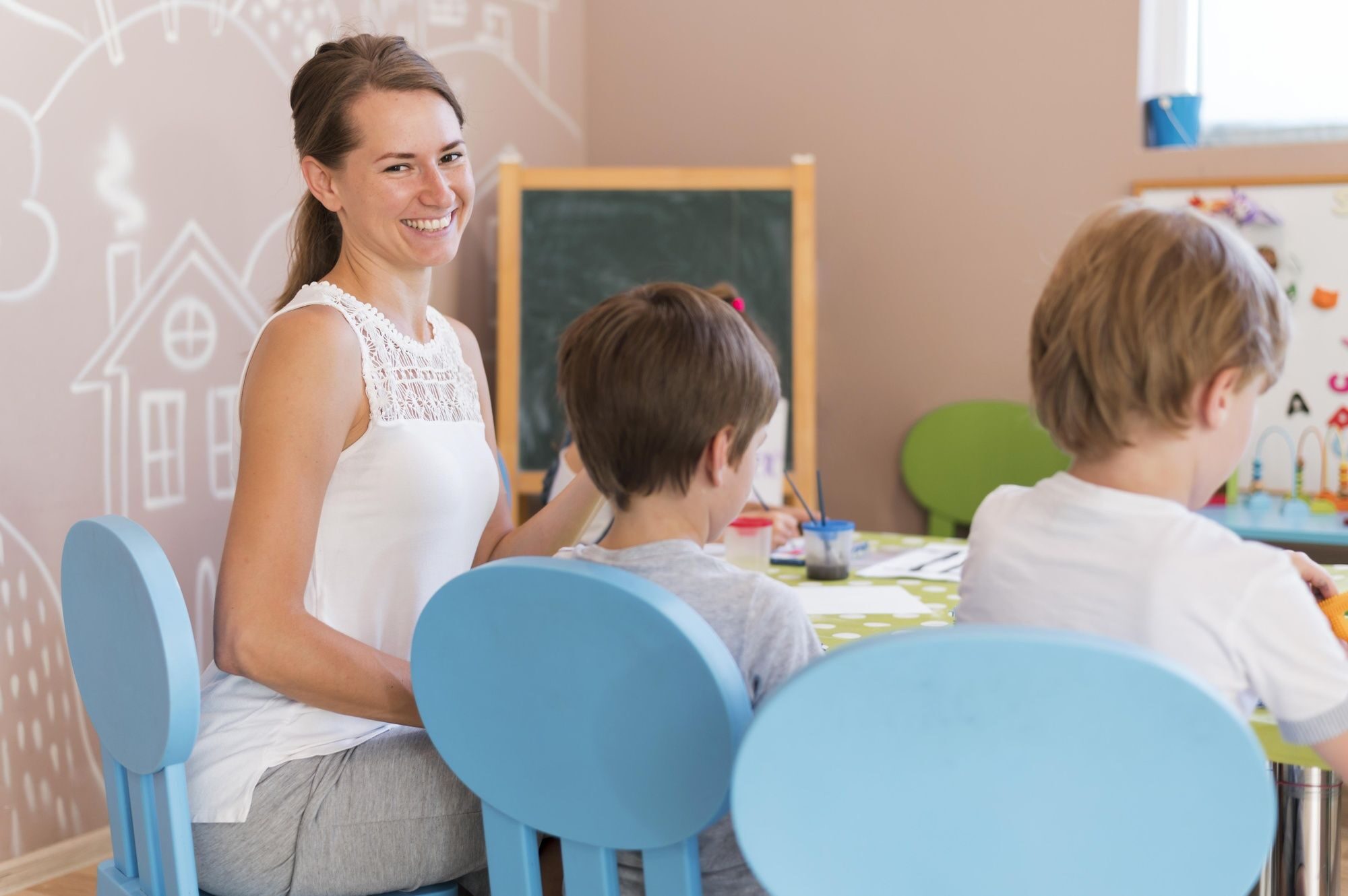 une femme souriante regarde l'objectif, assise à une table colorée à côté de deux jeunes enfants