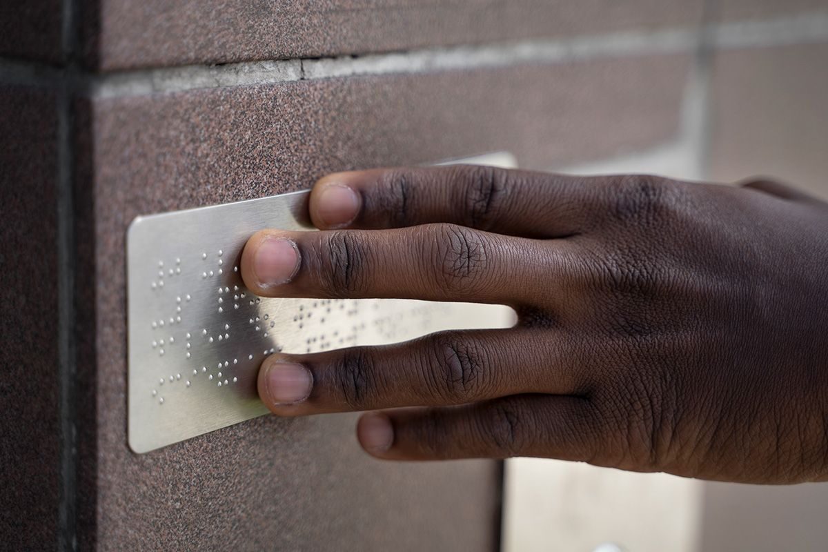 la main d'une personne noire posée sur une plaque métallique en braille - crédit photo : freepik